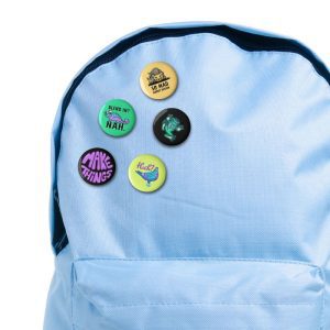 Mockup of five 32mm illustrated button badges arranged on back pack. Designs include a lion, chameleon, frog, pigeon in sneakers, and ‘Make Things’ lettering badge.